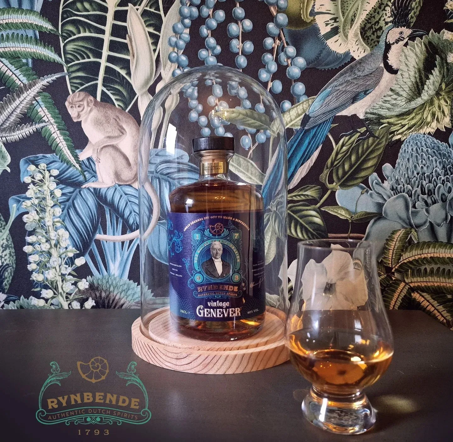 Rynbende bottle inside of a bell jar with next to it a glencairn glass filed with Rynbende. Both are on a bar and on the background jungle wallpaper is seen. Bottom left shows Rynbende' slogo
